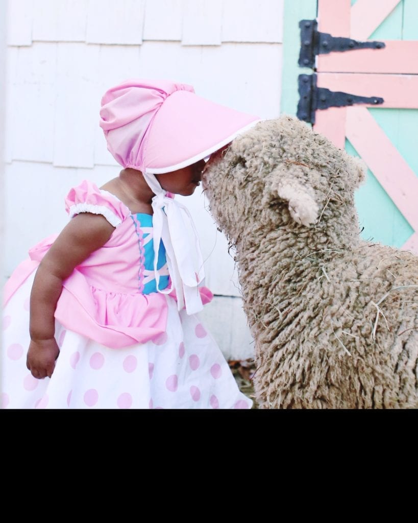 a toddler dressed as little bo peep kissing a sheep