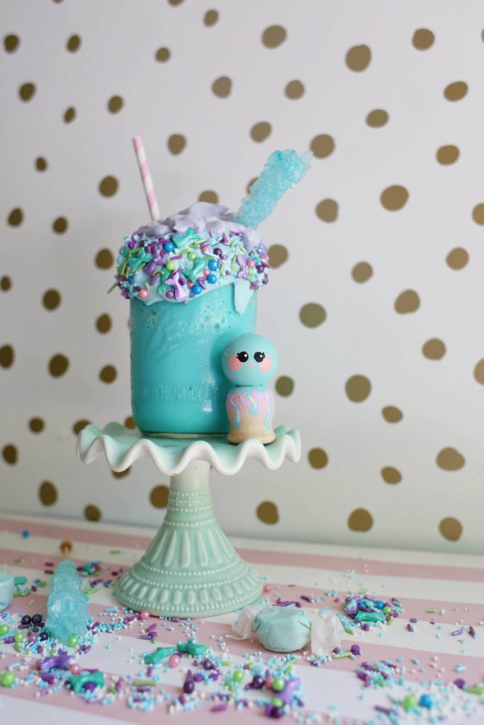 Blue Mermaid milkshake sitting next to a cute blue wooden doll 